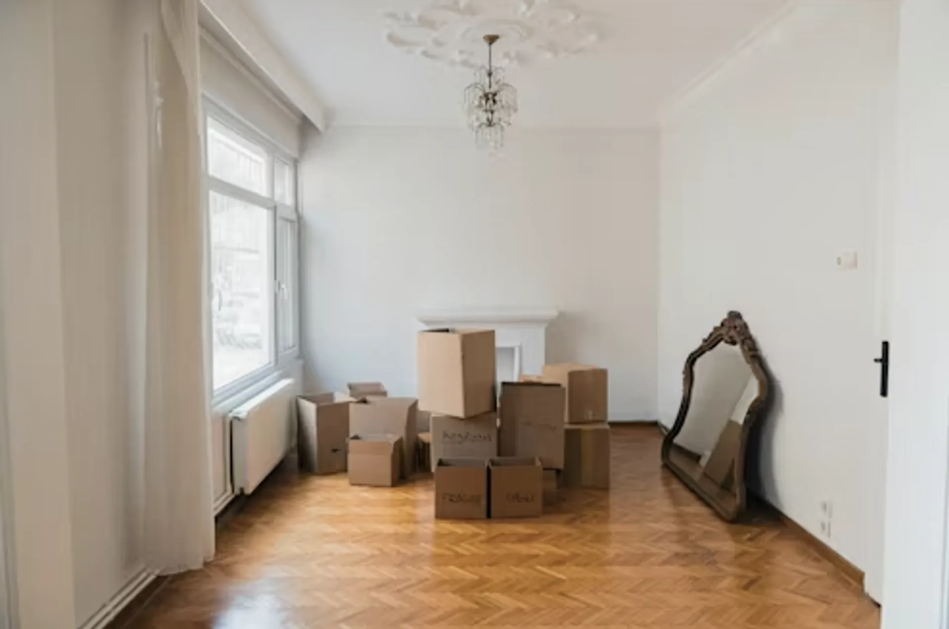 Séjour avec cartons de déménagement au sol et miroir contre le mur, cheminée masquée